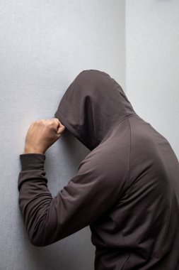 Gri başlıklı kızgın adam yumruğunu beyaz duvara çarpıyor.