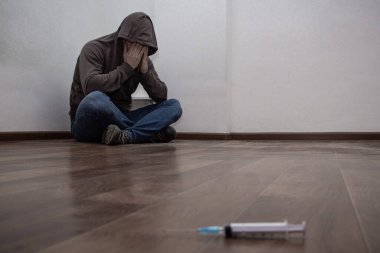 Odaklanmadan şırınga ve arka planda köşede oturan uyuşturucu bağımlısı adam. Kopyalama alanı ile