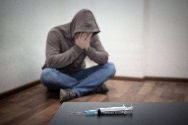 Şırınga ve adam uyuşturucu bağımlısı arkada köşede oturuyor. Kopyalama alanı ile