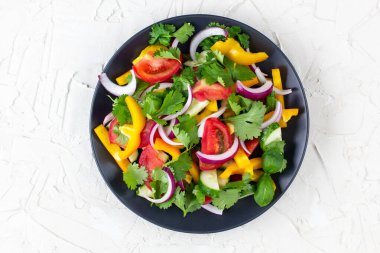 Farklı sebzelerle dolu bir tabak gökkuşağı salatası ve beyaz taş arka planda siyah tabakta otlar. Üst görünüm