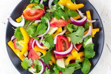 Farklı sebzelerle dolu bir tabak gökkuşağı salatası ve beyaz taş arka planda siyah tabakta otlar. Üst görünüm