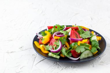 Farklı sebzelerle dolu bir tabak gökkuşağı salatası ve beyaz taş arka planda siyah tabakta otlar.