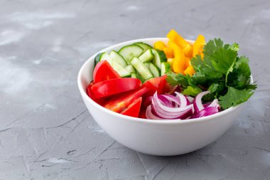 Farklı sebzelerle dolu bir tabak gökkuşağı salatası ve gri taş arka planda beyaz kâse içinde otlar. Kopyalama alanı ile