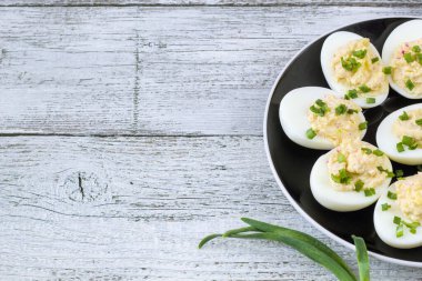 Yengeç çubuklu doldurulmuş yumurta, mayonez, peynir ve siyah tabakta yeşil soğan. Beyaz arkaplan