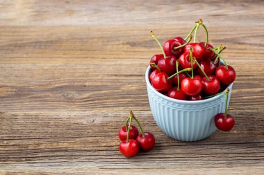 Olgun ıslak kirazlar mavi bir kasede damlalar ile ahşap arka planda kopyalanmış