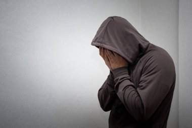 Gri başlıklı genç bir adamın portresi elleriyle yüzünü kapladı. Bağımlılık, alkolizm, depresyon ve umutsuzluk kavramı.