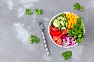 Farklı sebzelerle dolu bir tabak gökkuşağı salatası ve gri taş arka planda çatallı beyaz kâse içinde otlar. Kopyalama alanı olan üst görünüm