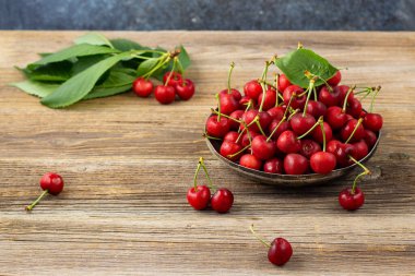 Olgun ıslak kirazlar ve yeşil yapraklar ahşap arka planda metal bir plaka.