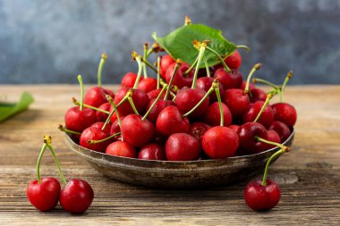Olgun ıslak kirazlar ve yeşil yapraklar ahşap arka planda metal bir plaka.