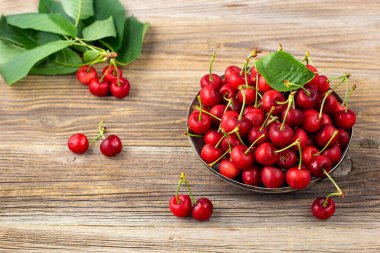 Olgun ıslak kirazlar ve yeşil yapraklar ahşap arka planda metal bir plaka.