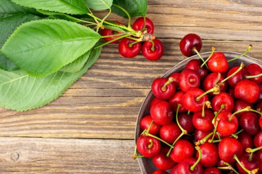 Tahta zemin üzerinde metal bir plaka içinde yeşil yapraklı olgun ıslak kirazlar. Kopyalama alanı olan üst görünüm
