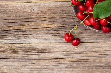 Olgun ıslak kirazlar ve yeşil yapraklar ahşap arka planda metal bir plaka.