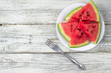 Olgun karpuz dilimleri beyaz ahşap arka planda çatalla tabakta