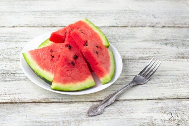 Olgun karpuz dilimleri beyaz ahşap arka planda çatalla tabakta