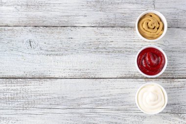 Beyaz ahşap arka planda üç çeşit klasik sos. Mayonez ketçap hardalı. Kopyalama alanı olan üst görünüm