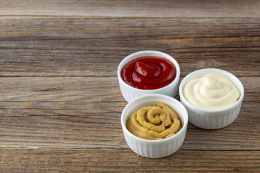 Doğal ahşap arka planda üç çeşit klasik sos. Mayonez ketçap hardalı. Kopyalama alanı olan üst görünüm