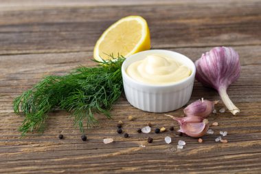 Doğal ahşap arka planda sarımsak, yumurta, yağ ve bitkilerle mayonez sosu.