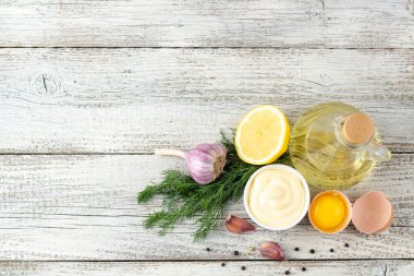 Beyaz ahşap arka planda sarımsak, yumurta, yağ, limon ve otlu mayonez sosu.