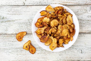 Ahşap arka planda beyaz bir tabakta dilimlenmiş kuru armut yığını. Kurutulmuş meyve cipsi. Sağlıklı yiyecekler. Üst görünüm