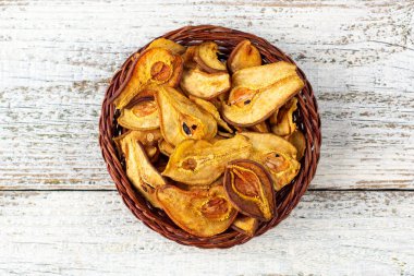 Beyaz ahşap arka planda hasır sepette kurumuş armut dilimleri yığını. Kurutulmuş meyve cipsi. Sağlıklı yiyecekler. Üst görünüm