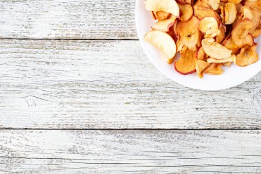 Ahşap arka planda beyaz bir tabakta dilimlenmiş bir yığın kuru elma. Kurutulmuş meyve cipsi. Sağlıklı yiyecekler. Kopyalama alanı olan üst görünüm