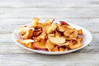 Ahşap arka planda beyaz bir tabakta dilimlenmiş bir yığın kuru elma. Kurutulmuş meyve cipsi. Sağlıklı vejetaryen yemekleri