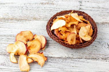 Hasır sepette beyaz ahşap arka planda kurumuş elma dilimleri yığını. Kurutulmuş meyve cipsi. Sağlıklı yiyecekler. Üst görünüm