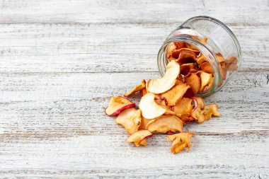 Beyaz ahşap arka planda cam bir kavanozdan alınmış kurumuş elma hapları yığını. Kurutulmuş meyve cipsi. Sağlıklı vejetaryen yemekleri