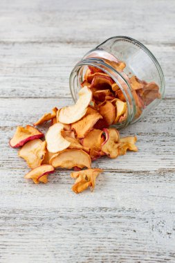 Beyaz ahşap arka planda cam bir kavanozdan alınmış kurumuş elma hapları yığını. Kurutulmuş meyve cipsi. Sağlıklı vejetaryen yemekleri