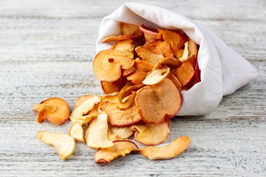 Ahşap arka plandaki beyaz bir keseden alınmış kurumuş elma hapları yığını. Kurutulmuş meyve cipsi. Sağlıklı vejetaryen yemekleri