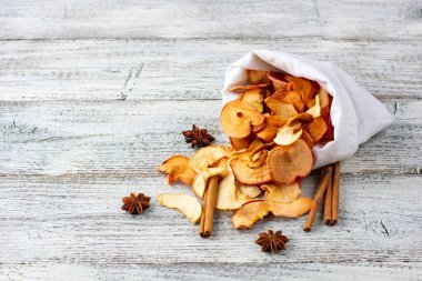 Ahşap arka plandaki beyaz bir keseden bir yığın kurutulmuş elma ve baharat hapı. Kurutulmuş meyve cipsi. Sağlıklı vejetaryen yemekleri