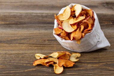 Ahşap arka plandaki beyaz bir keseden alınmış kurumuş elma hapları yığını. Kurutulmuş meyve cipsi. Sağlıklı vejetaryen yemekleri