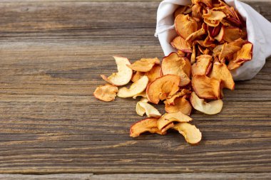 Ahşap arka plandaki beyaz bir keseden alınmış kurumuş elma hapları yığını. Kurutulmuş meyve cipsi. Sağlıklı vejetaryen yemekleri