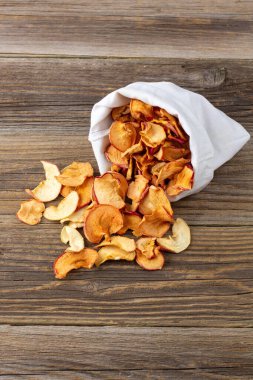 Ahşap arka plandaki beyaz bir keseden alınmış kurumuş elma hapları yığını. Kurutulmuş meyve cipsi. Sağlıklı vejetaryen yemekleri