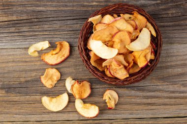 Tahta arka planda hasır sepette kurumuş elma dilimleri yığını. Kurutulmuş meyve cipsi. Sağlıklı yiyecekler. Üst görünüm