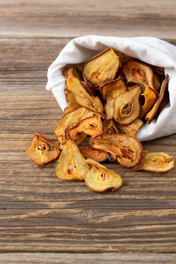 Ahşap arka plandaki beyaz bir keseden bir yığın kurutulmuş armut hapı. Kurutulmuş meyve cipsi. Sağlıklı vejetaryen yemekleri