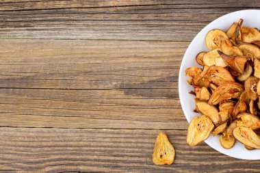Ahşap arka planda beyaz bir tabakta dilimlenmiş kuru armut yığını. Kurutulmuş meyve cipsi. Sağlıklı yiyecekler. Kopyalama alanı olan üst görünüm