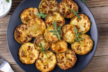 Ekşi krema soslu kızarmış kabak dilimleri. Doğal kahverengi ahşap arka planda akşam yemeği için otlu kızarmış kabaklar. Üst Wiev