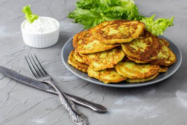 Ekşi krema soslu ve yeşillikli kabaklı börekler. Gri arka planda yeşil salatalı kabak krepleri..