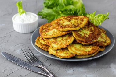 Ekşi krema soslu ve yeşillikli kabaklı börekler. Gri arka planda yeşil salatalı kabak krepleri..