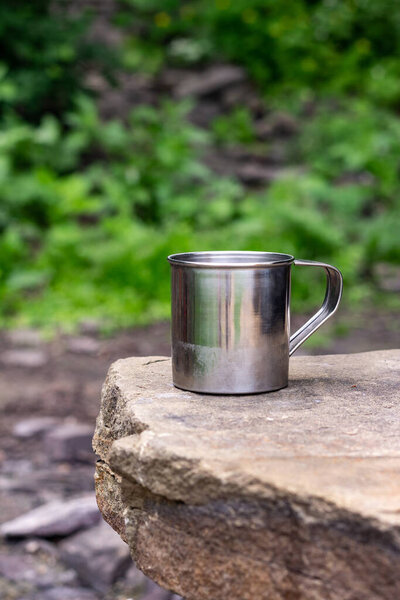 Stainless camping mug stands on the stones on front of natural green with copy space