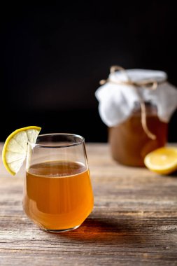 Çiğ mayalanmış ev yapımı alkolik ya da alkolsüz kombu çayı. Buzlu çay ve sağlıklı probiyotik bardakta ve ahşap arka planda limon dilimi.