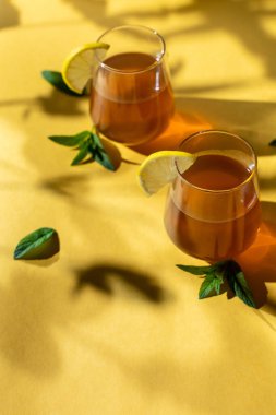 Çiğ mayalanmış ev yapımı alkolik ya da alkolsüz kombu çayı. Buzlu çay ve bardakta doğal probiyotik, limon dilimi ve sarı arka planda nane. Sert gölge