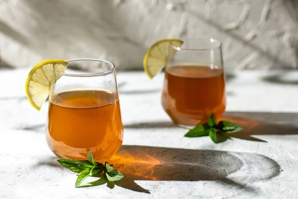 Raw fermented homemade alcoholic or non alcogolic kombucha superfood. Ice tea with healthy natural probiotic in glass with lemon slice and mint on white background. Hard shadow
