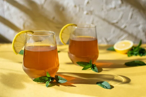 Raw fermented homemade alcoholic or non alcogolic kombucha superfood. Ice tea with healthy natural probiotic in glass with lemon slice and mint on yellow background. Hard shadow