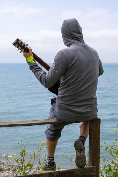 코카서스 젊은이가 바다의 해안에서 기타를 연주하고 있었습니다 뒤에서 — 스톡 사진