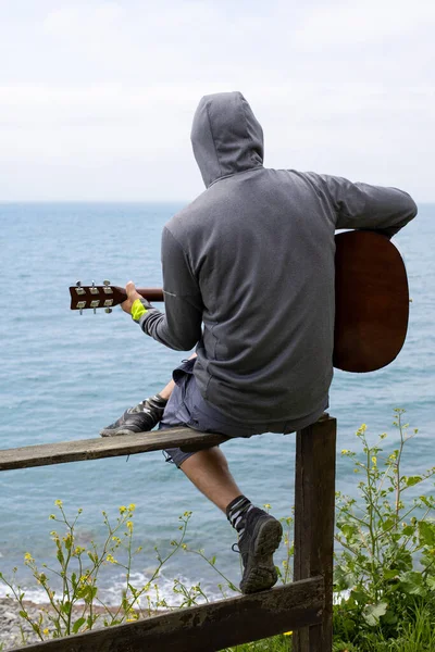 코카서스 젊은이가 바다의 해안에서 기타를 연주하고 있었습니다 뒤에서 — 스톡 사진