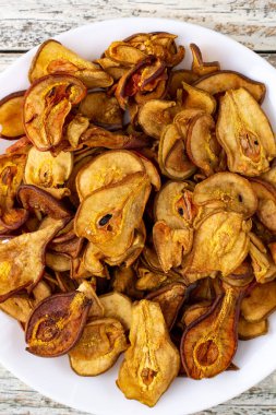 Ahşap arka planda beyaz bir tabakta dilimlenmiş kuru armut yığını. Kurutulmuş meyve cipsi. Sağlıklı yiyecekler. Üst görünüm