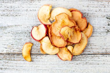 Beyaz ahşap arka planda dilimlenmiş kurumuş elma yığını. Kurutulmuş meyve cipsi. Sağlıklı yiyecekler. Üst görünüm