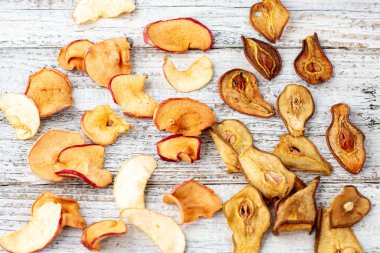 Beyaz ahşap arka planda dilimler halinde kurumuş armut ve elma deseni. Kurutulmuş meyve cipsi. Sağlıklı yiyecekler. Üst görünüm